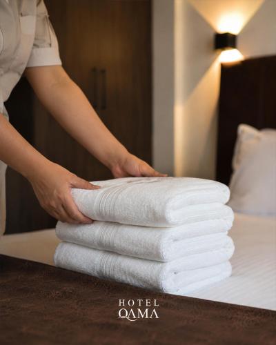 a person is stacking white towels on a bed at Qama Hotel in Prishtinë