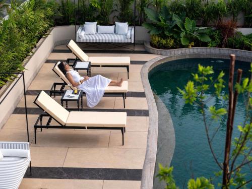 a woman laying on a chair next to a swimming pool at Pullman Chennai Anna Salai - Premium Brand By Accor in Chennai