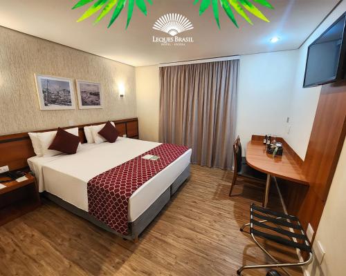 a hotel room with a bed and a desk and a television at Leques Brasil Hotel Escola in São Paulo