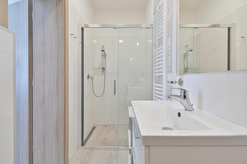 a white bathroom with a shower and a sink at Apartmán na výsluní in Luhačovice