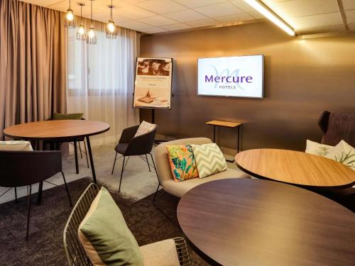 a waiting room with tables and chairs and a tv at Hôtel Mercure Lyon Centre Lumière in Lyon