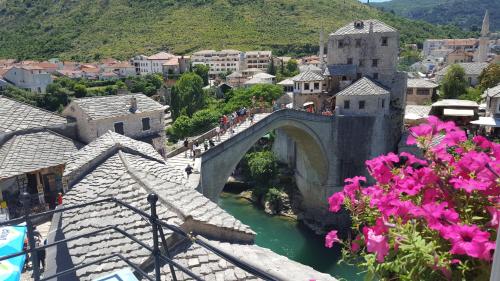 a bridge over a river in a town with pink flowers at Hotel Amicus in Mostar