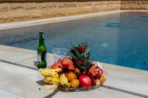 a bowl of fruit and a bottle of wine next to a pool at منتجع ليورا ــ Liora Resort in Al Ḩanī