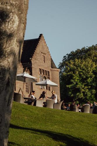 people sitting at tables with umbrellas in front of a building at Murrayshall Country Estate in Perth