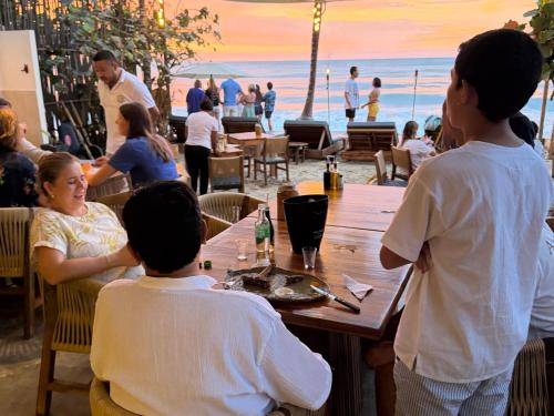 a group of people sitting at a table at the beach at Makao Beach Hotel in Palomino