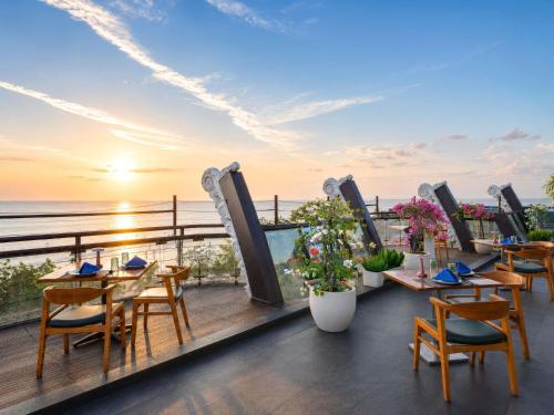 a restaurant with tables and chairs on a balcony overlooking the ocean at The Kuta Beach Heritage Hotel - Managed by Accor in Kuta