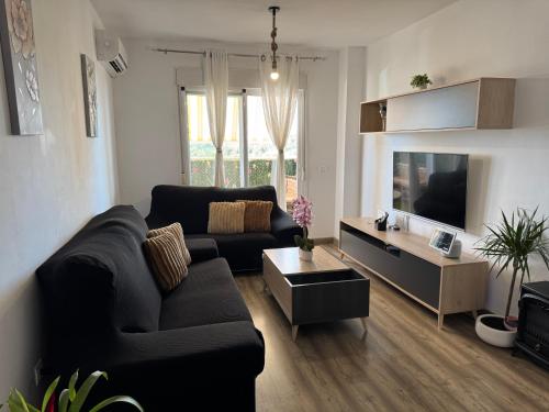 a living room with a black couch and a tv at Acogedor Apartamento in Almerimar