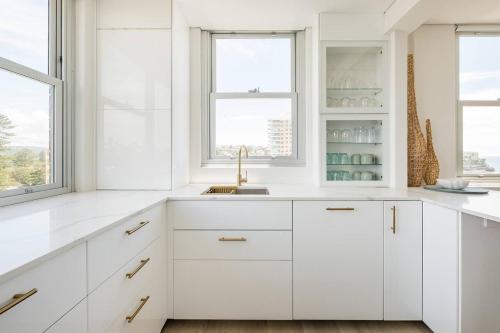 a white kitchen with white cabinets and a sink at Stunning Beachfront penthouse-Beach District Views in Sydney