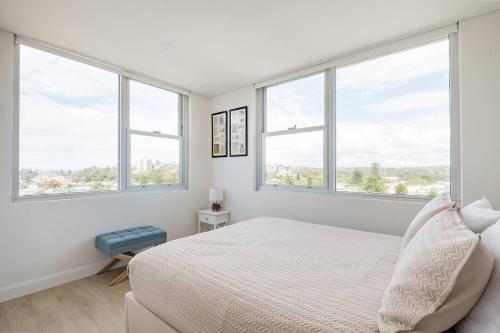 a white bedroom with windows and a bed at Stunning Beachfront penthouse-Beach District Views in Sydney
