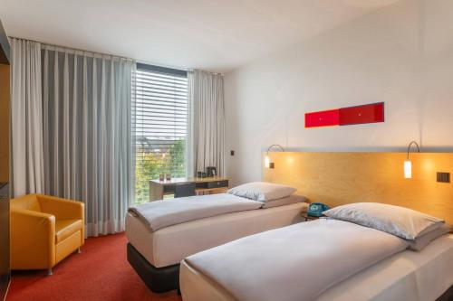 a hotel room with two beds and a chair at INNSiDE by Meliá Düsseldorf Seestern in Düsseldorf