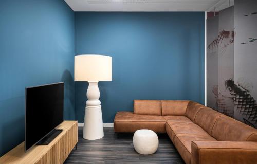 a living room with a brown couch and a television at elaya hotel augsburg, Trademark by Wyndham in Augsburg