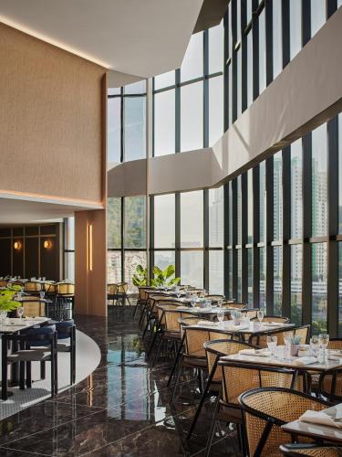 a restaurant with tables and chairs and large windows at Harris Hotel & Conventions Sunshine Penang in Ayer Itam