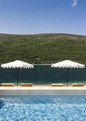 two white umbrellas and chairs next to a swimming pool at One&Only Portonovi in Herceg-Novi