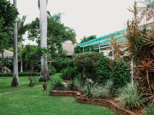 a garden with palm trees and plants in front of a house at El Palmar Guesthouse in Groblersdal