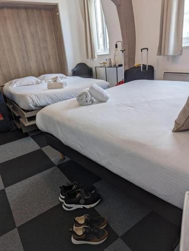 two beds in a hotel room with shoes on the floor at Le Lion dOr Hôtel de Charme et centre ville de Bernay in Bernay