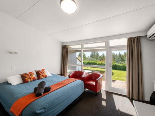 a bedroom with a bed and a chair and a window at Taupo Debretts Spa Resort in Taupo