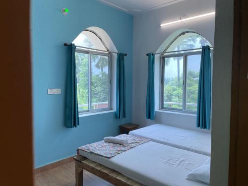 two beds in a room with two windows at Senamura Yoga Ashram Guesthouse in Bodh Gaya