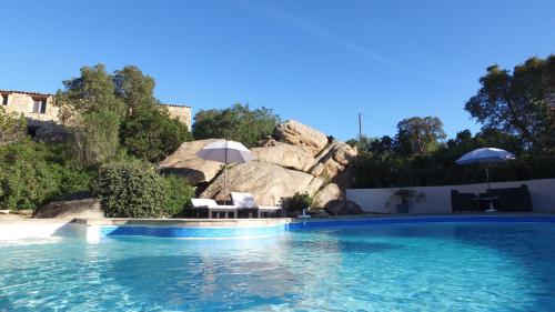 - une piscine avec des chaises et des parasols en face d'un rocher dans l'établissement residence stella d'oro, à Porto-Vecchio