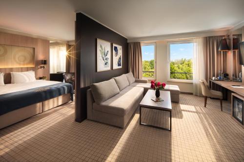 a hotel room with a couch and a bed and a desk at Landmark Creek Hotel & Wellness Plovdiv in Plovdiv