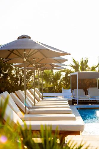 a row of white lounge chairs under an umbrella next to a pool at San Marco Hotel and Villas in Houlakia
