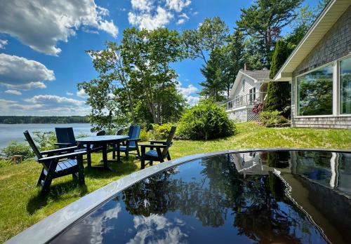 a patio with a table and chairs next to a body of water at Lucky Stone Retreat - private beach & Acadia view in Sullivan