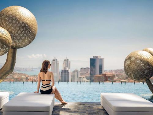 a woman in a bikini sitting on a couch by the water at Fairmont Quasar Istanbul Hotel in Istanbul