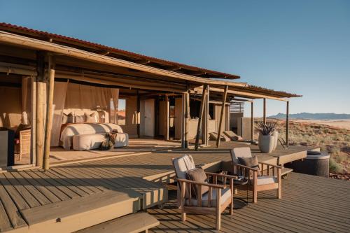 a bed and two chairs on a wooden deck at Wolwedans Desert lodge in NamibRand