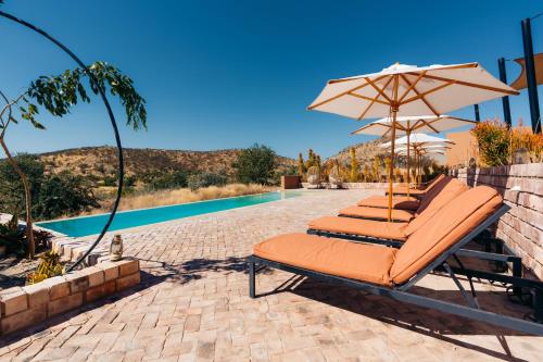a group of lounge chairs with an umbrella next to a pool at Lodge Damaraland in Khorixas