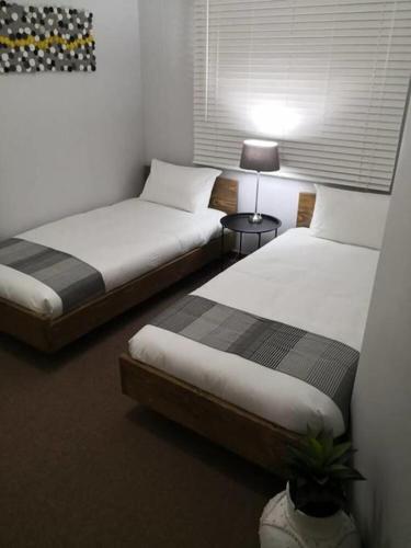 two beds in a room with two tables and a lamp at Place At Menlyn in Pretoria