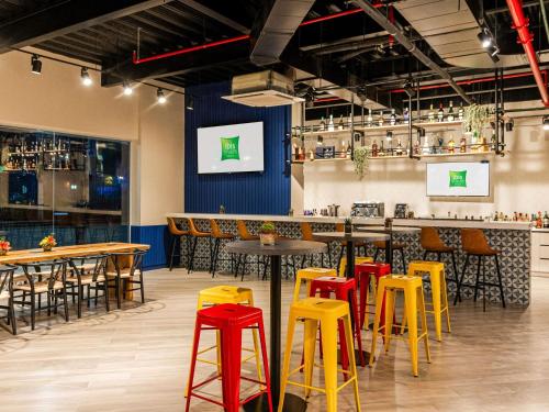 a bar with yellow and red stools in a room at Ibis Styles El Malecon Guayaquil in Guayaquil