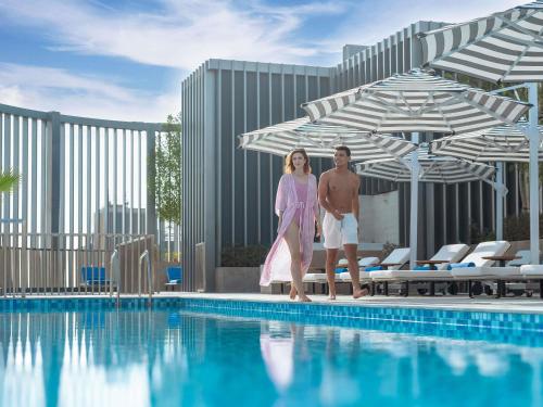 a man and a woman standing next to a swimming pool at Mercure Dubai Deira in Dubai