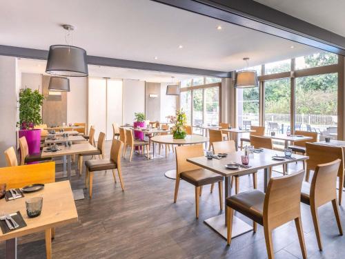 a restaurant with tables and chairs and windows at Mercure Strasbourg Aéroport in Ostwald
