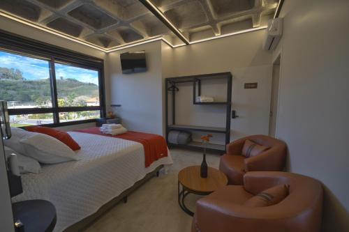 a bedroom with a bed and a chair and a window at Pousada Premium Terragnolo in Bento Gonçalves