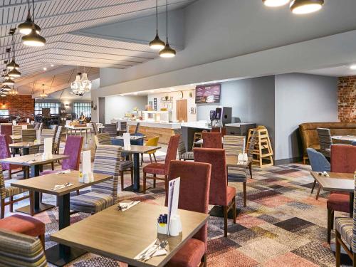 a restaurant with wooden tables and chairs and a cafeteria at Novotel Manchester West in Worsley