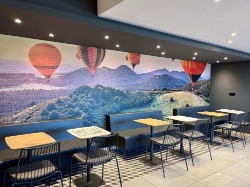 a restaurant with tables and chairs and a mural of hot air balloons at ibis Clermont Ferrand Montferrand in Clermont-Ferrand