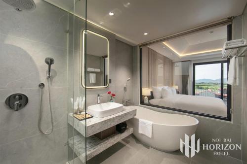 a bathroom with a tub and a sink and a bed at Noi Bai Horizon Hotel & Spa in Noi Bai