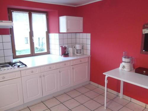 une cuisine avec des placards blancs et un mur rouge dans l'établissement Gite le Sauceley Maison de vacances pour 6 à 10 personnes, à Girmont-Val-d'Ajol