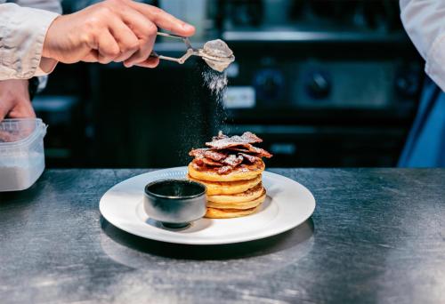 a person is sprinkling powdered sugar on a stack of pancakes at Radisson Blu Royal Garden Hotel, Trondheim in Trondheim