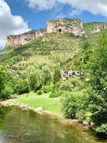 a house on the side of a river with a mountain at La Caze in Saint-Pierre-des-Tripiers