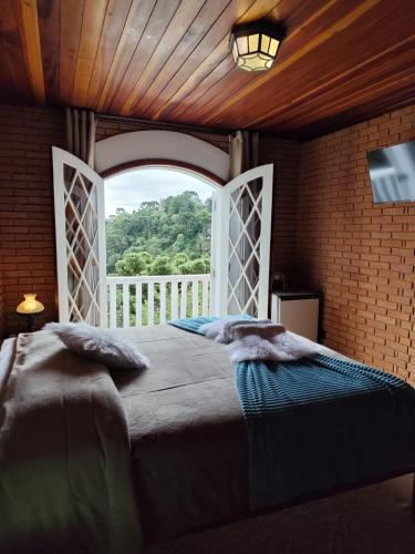 a bedroom with a large bed with a large window at Refugio maná in Campos do Jordão