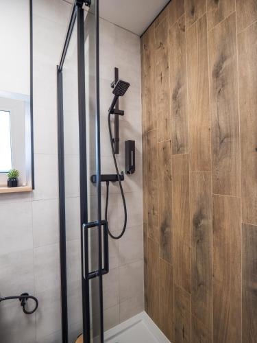 a shower in a bathroom with a wooden wall at SierPlejs Hill - domki przy szlaku w Górach Sowich in Sierpnica