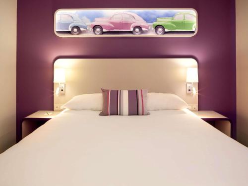 a bedroom with a large bed with two cars on the wall at ibis Styles Montbéliard in Montbéliard