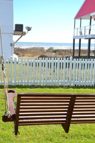 a wooden bench next to a white fence and the beach at Pelican Path in Galveston