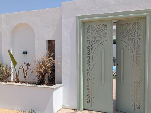 a pair of doors on a white building with plants at Villa SUN SQUARE DJERBA in Awlād ‘Umar