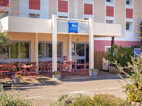 a hotel with tables and chairs in front of a building at Ibis Budget Fréjus Capitou in Fréjus