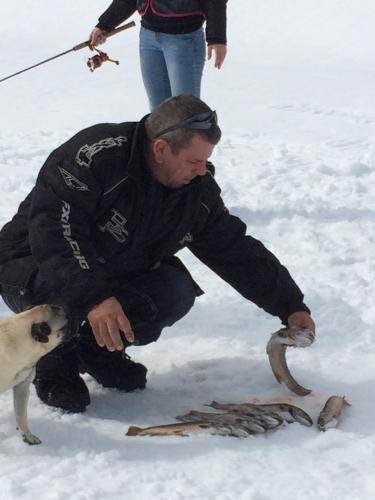 a man holding a fish in the snow with a dog at domaine de la vallee in Sainte-Rose-du-Nord