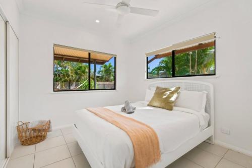 a white bedroom with a bed with two windows at The Beachwood Nest in Broome