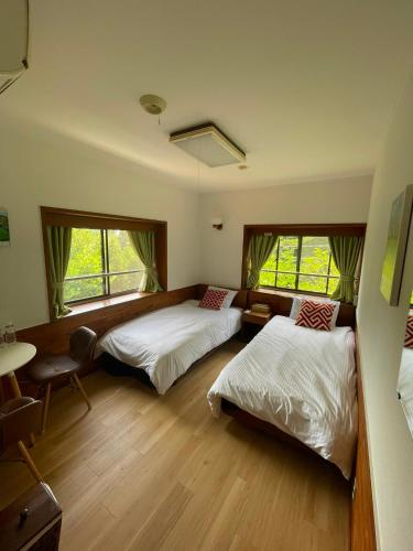 a bedroom with two beds and a table and two windows at Shika Lodge Izu in Ito