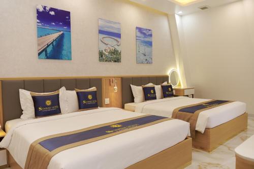 two beds in a hotel room with paintings on the wall at Sunrise Hotel Phước Kim in Bạc Liêu