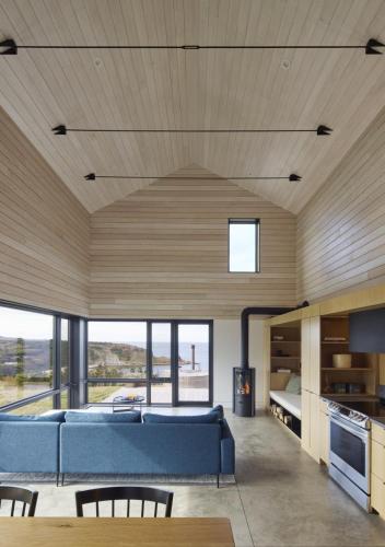 a living room with a blue couch and some windows at Cedar - Luxury Oceanview Cottage with Hot Tub & Private Beach Access near Cabot Trail in Chimney Corner